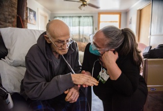 A nurse leans down and speaks to a patient sitting in a chair.