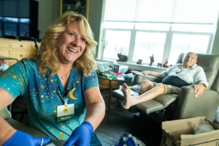 A nurse smiles as a patient sits in a chair with his legs propped up.