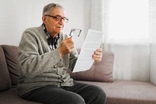 An elder gentleman uses a magnifying glass to read a piece of paper.