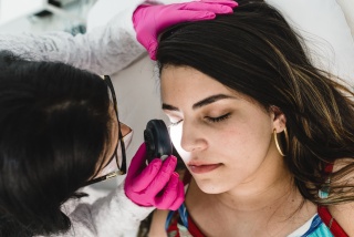 A medical provider shines a light on a patient's face during a skin check.