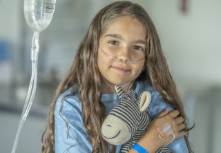 A child stares at the camera while holding a stuffed animal.