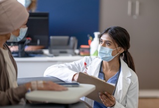 A medical provider kneels while speaking with a patient.
