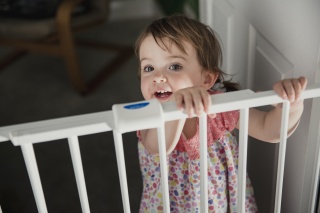 A child stands behind a protective gate enabled to prevent fall injuries.