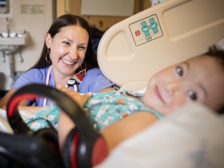 Megan Prue, MD, smiles while speaking to a pediatric patient in their hospital room at Golisano Children's Hospital.