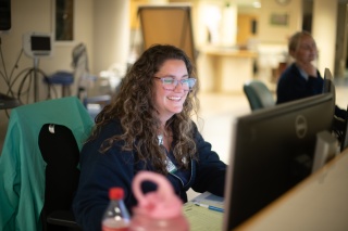 Smiling hospital staff member working at a computer at a nurses' station.