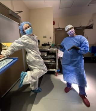 Two OBGYN residents in surgical gowns and masks pose playfully in the hospital.