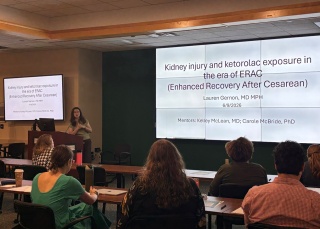 OBGYN resident presents research finding via a Powerpoint to a room of people.