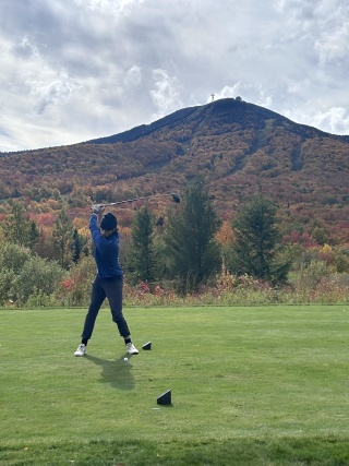 Austin Snyder swinging a golf club on an autumn day with the mountains in the backgroun/ 