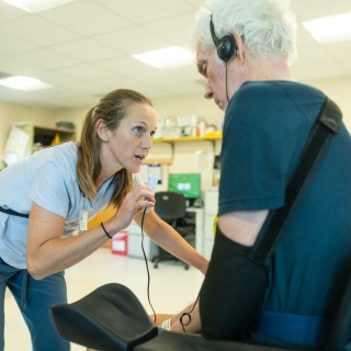A patient listens through headphones to a rehabilitation therapist speaking.