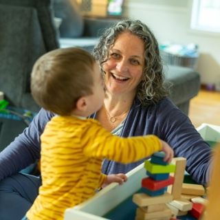 A Home Health and Hospice Occupational Therapist smiles at a child playing with blocks.