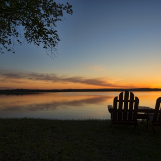 Two empty adirondack changes on shore facing sunset on lake