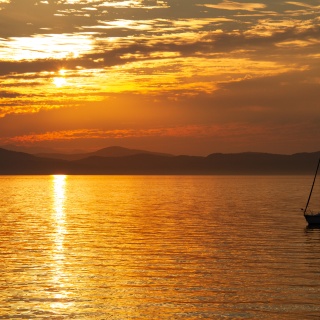 A sailboat silhouetted against sunset over lake with mountains in the background