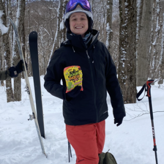 Susan Campbell, MD standing in snow holding bag of sour patch candy, her skis lodged in snow