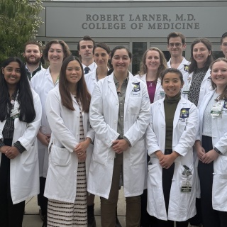 Group photo of surgical residents in their white coats standing at the Robert Larner, MD, College of Medicine entrance.